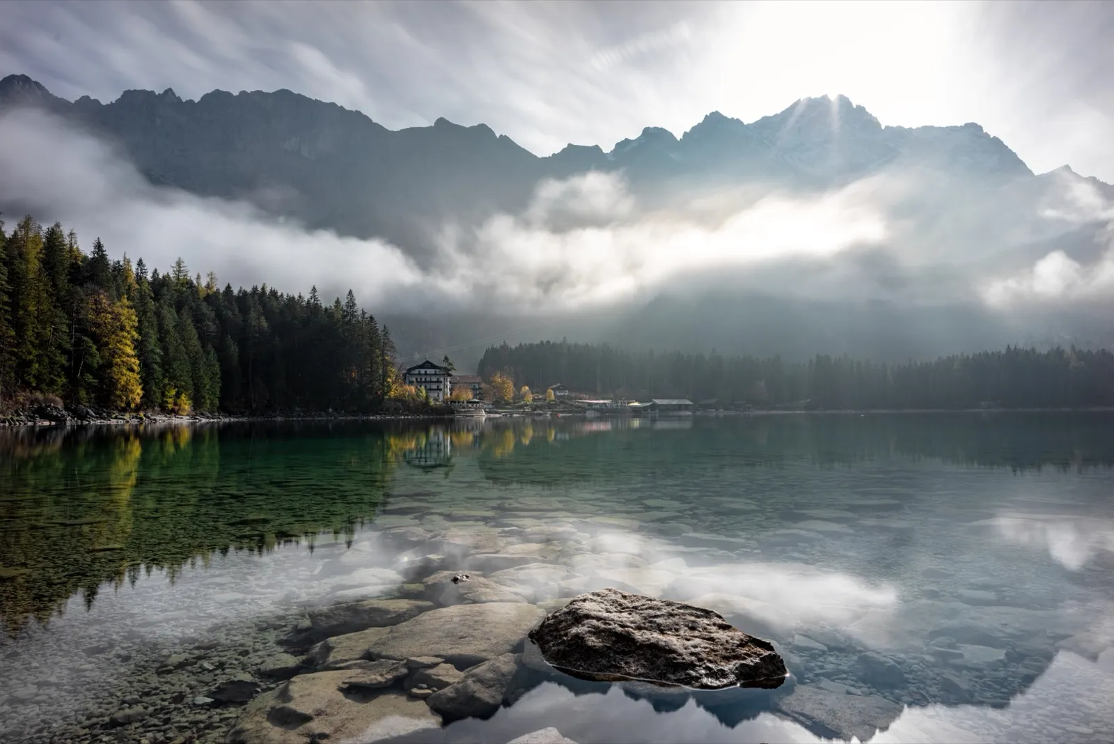 Un lago di montagna con nubi basse e bosco sulle rive