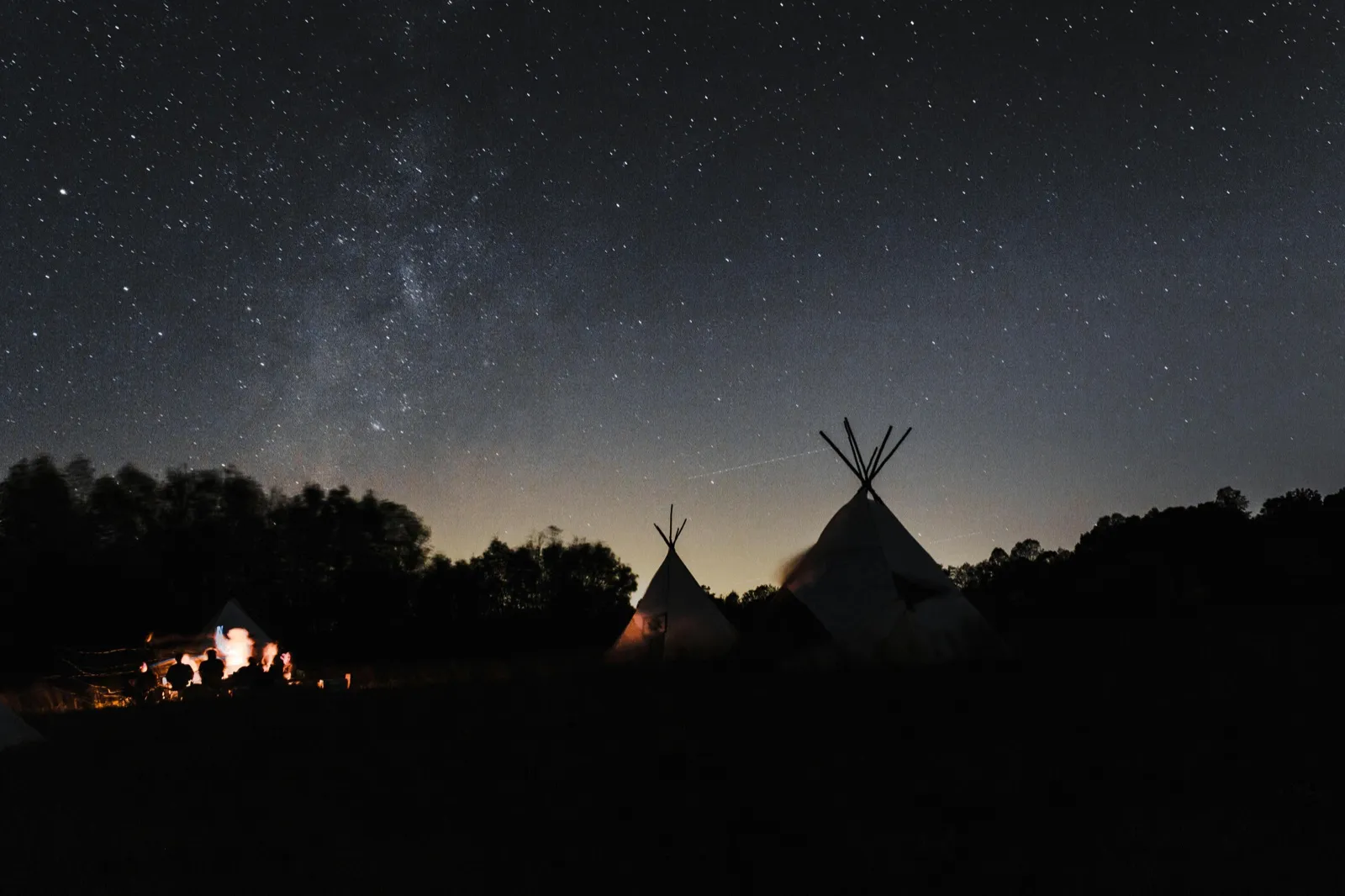Un cielo stellato sopra alcuni teepee e un falò