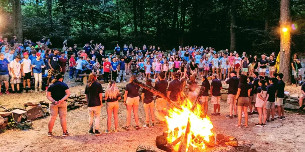 Un gruppo numeroso attorno a un falò nel bosco, al tramonto