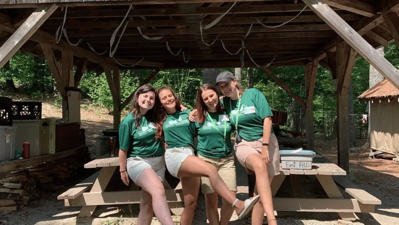 Tre ragazze in maglietta verde sedute su una panchina di legno sotto una tettoia