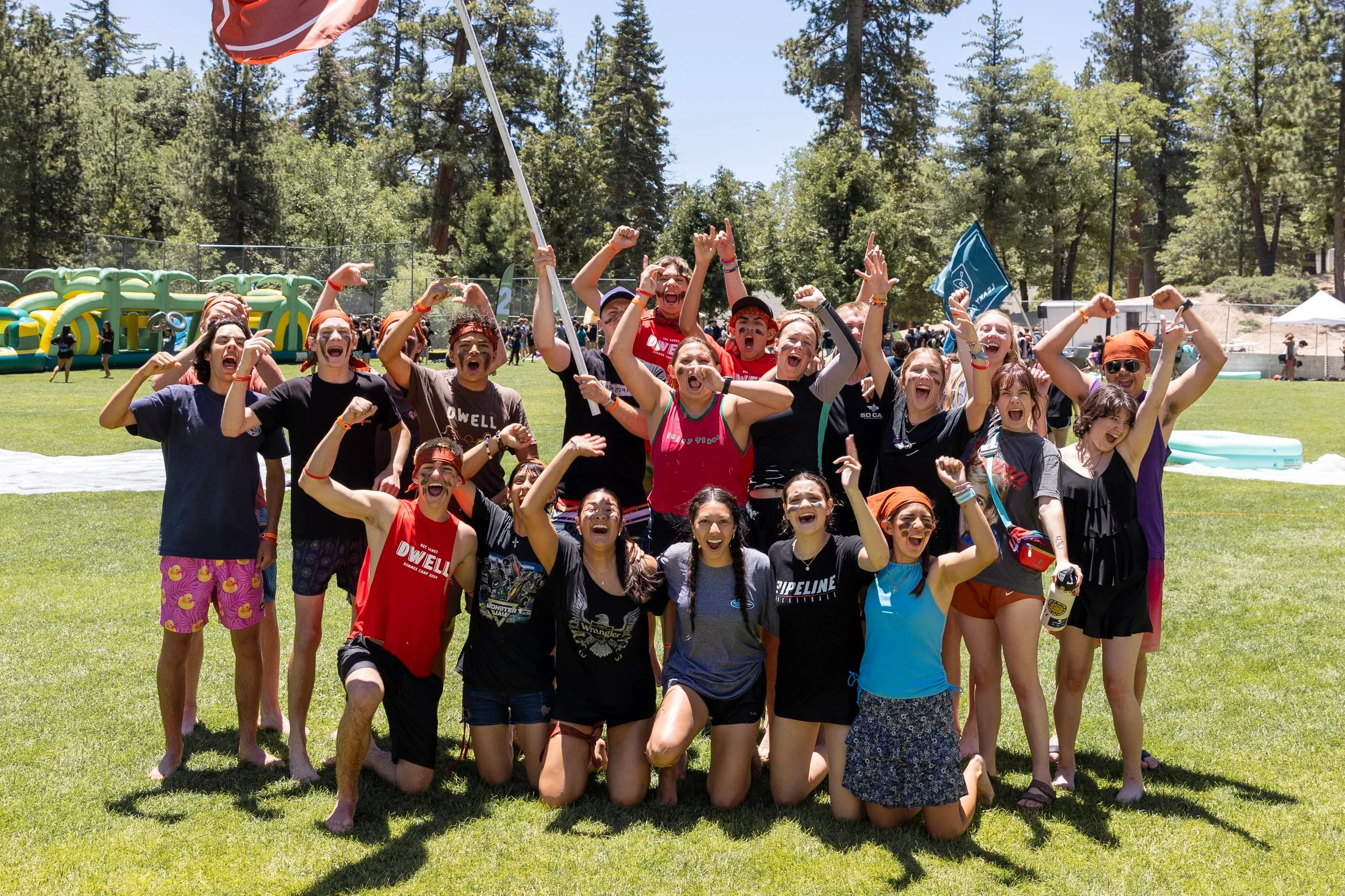 Un gruppo numeroso di counselor in una radura, con le braccia alzate, bosco sullo sfondo
