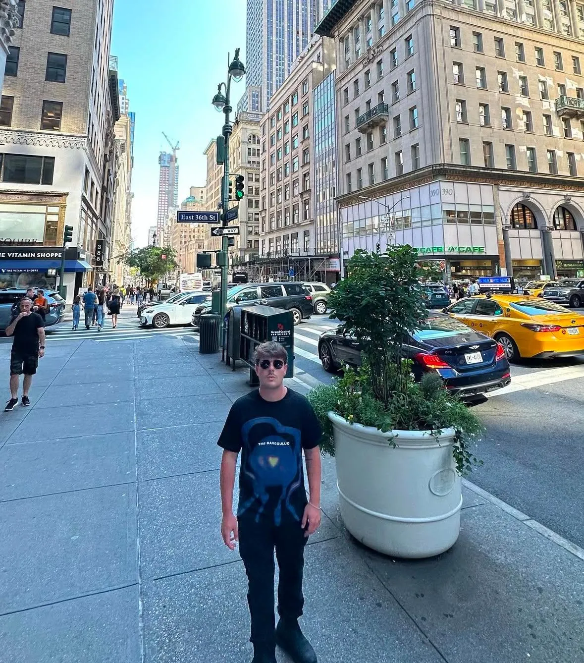 Un ragazzo su un marciapiede di New York, taxi gialli alle spalle